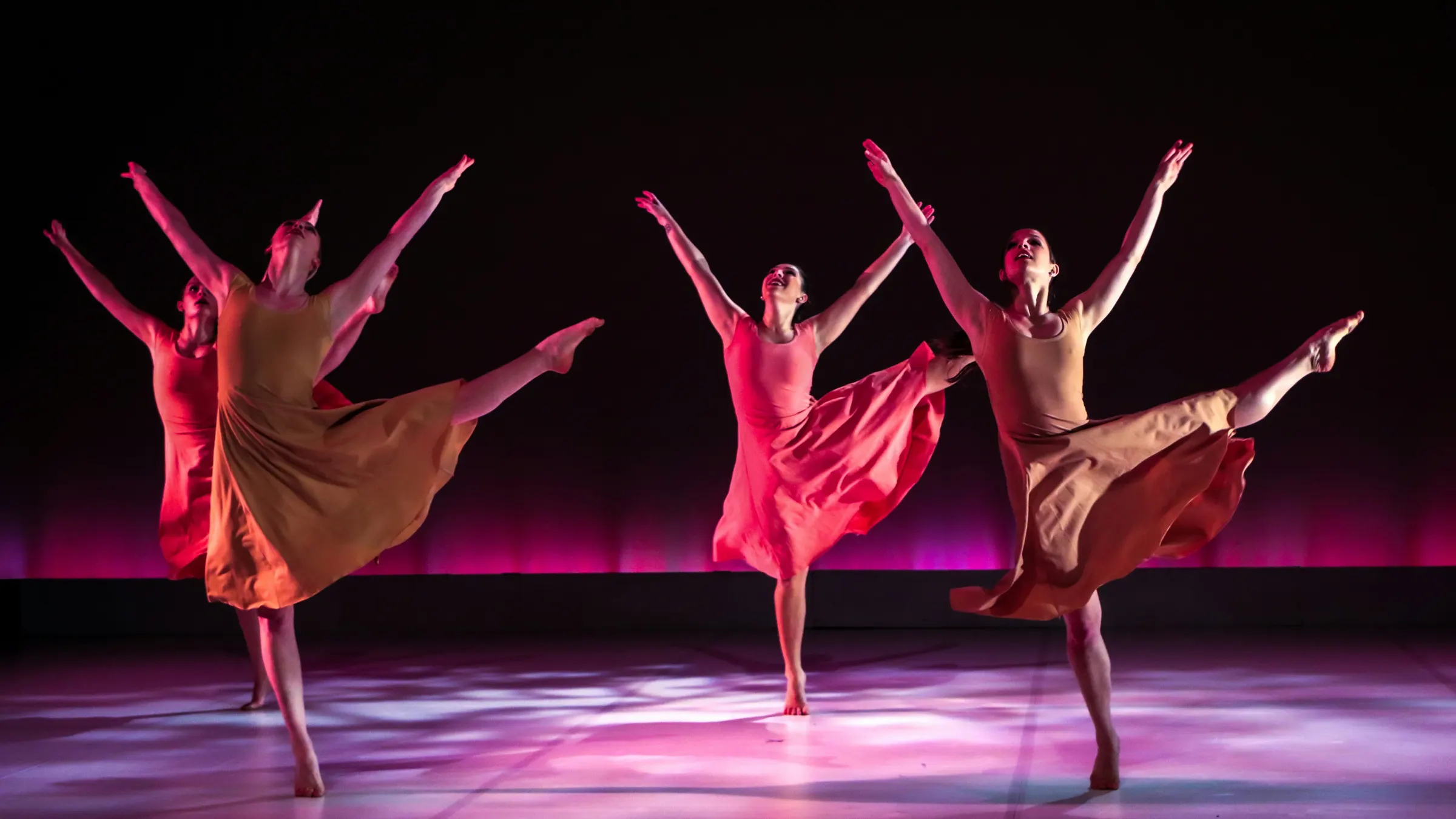 Four dancers leaping in unison under magenta stage light